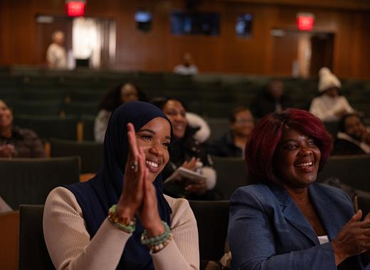 Black women sitting in an auditorium, smiling and clapping