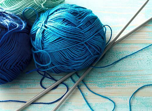 several blue yarn balls in various shades on a blue wood table with silver knitting needles sitting at an angle